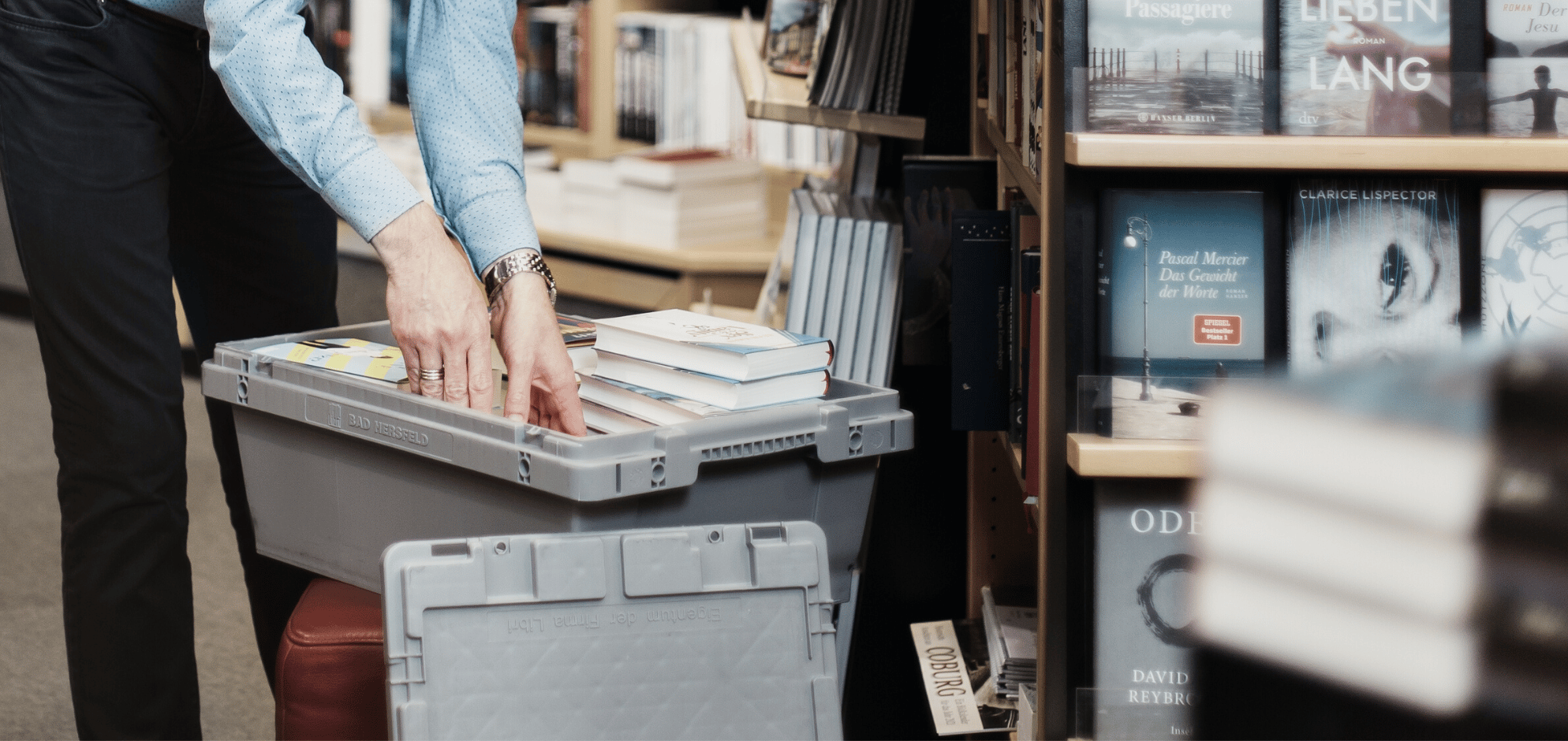 Hände packen eine Behälter mit Büchern aus.