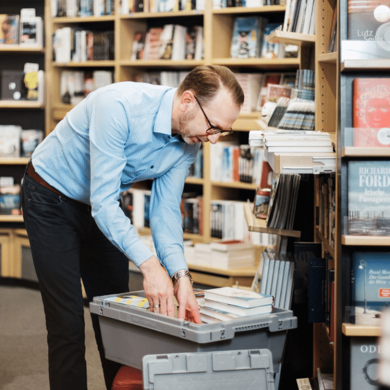Buchhändler beugt sich über die Libri Buchwanne.